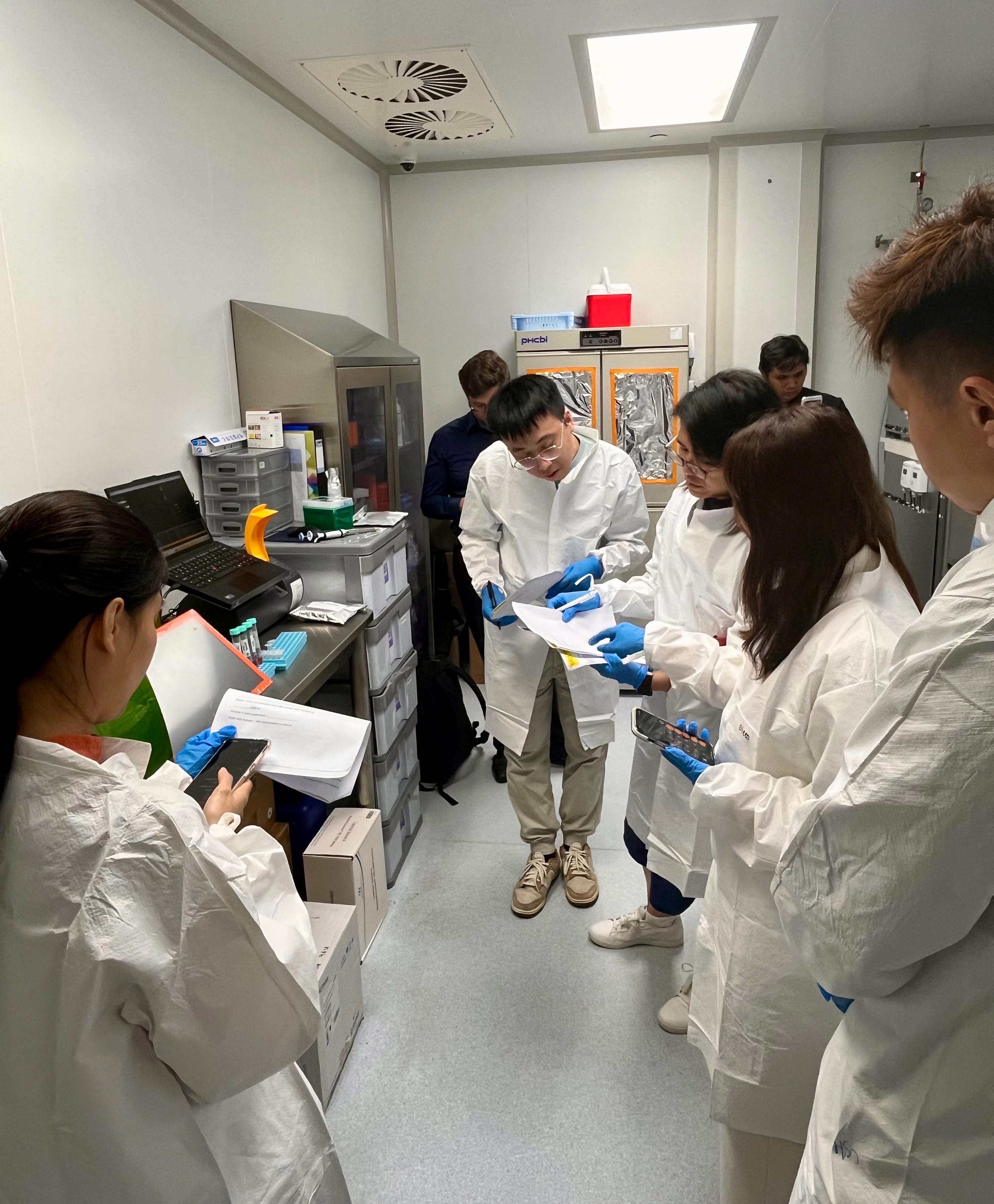 Participants in laboratory protective attire reviewing experimental procedures and recording observations during a hands-on cell culture training session in a research laboratory.